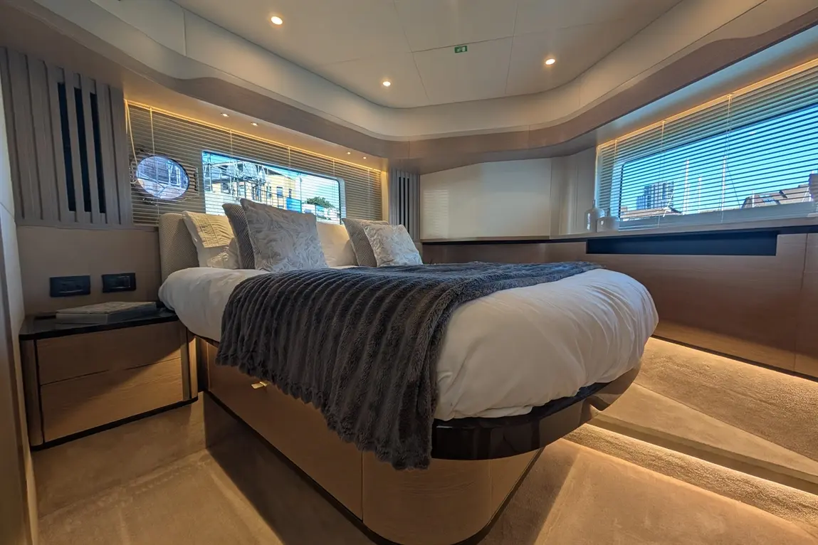 Luxury bedroom featuring a double bed with plush pillows and a grey throw, large windows with wooden blinds, and warm lighting.